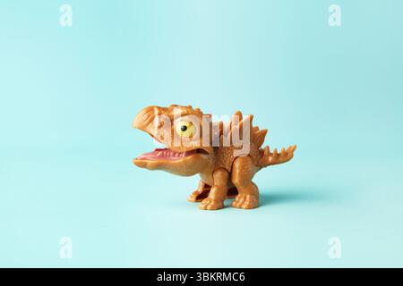Kleines und niedliches Plastik-Stiegosaurus-Spielzeug in Aktion auf cyanfarbenem Hintergrund Stockfoto
