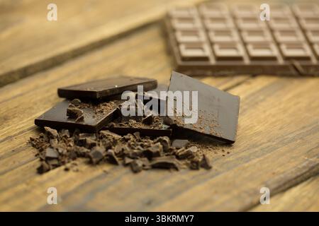 Dunkle Schokoladenstücke liegen auf einer Holzplatte in flachem Design mit verschwommenem Schokoladenriegel Stockfoto
