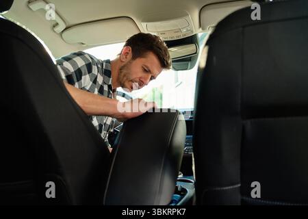 Mann in kariertem Hemd, der den vorderen Innenraum eines modernen Autos überprüft Stockfoto