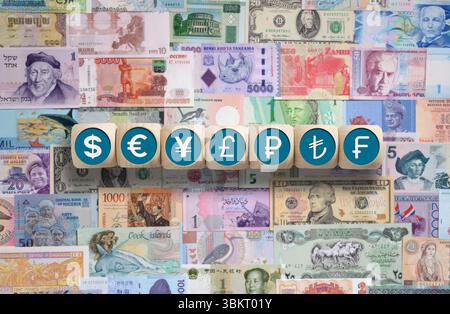 Holzwürfel mit Dollar, Euro, Yen, Pfund, Rubel, Lira- und Franc-Symbole, die auf einem Hintergrund von Banknoten aus der ganzen Welt platziert werden Stockfoto