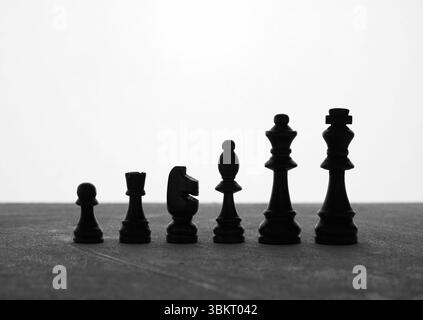 Silhouetten von Schachfiguren, die auf einer grauen Oberfläche vor weißem Hintergrund angeordnet sind, stehen für Strategie, Wettbewerb und Führung Stockfoto