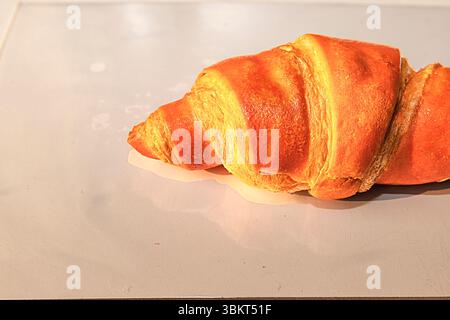 Nahaufnahme eines frisch gebackenen goldenen Croissants auf einem weichen hellen Hintergrund. Minimalistisches Essen, perfekt für Backwaren und Frühstücksthemen. Stockfoto