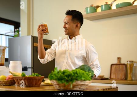 Ein lächelnder Mann hält ein Glas frisch gemischten Smoothie in der modernen Küche Stockfoto
