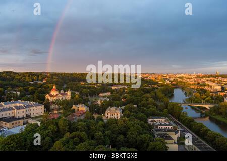 Ein atemberaubender Blick aus der Luft auf Vilnius bei Sonnenuntergang, mit einem Regenbogenbogen über der historischen Stadt, üppigem Grün und reflektierendem Fluss Neris Stockfoto