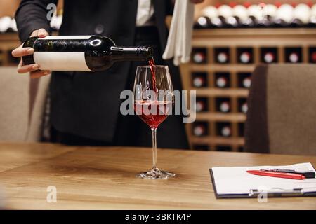 Sommelier, der Rotwein aus der Flasche in das Glas gießt, im Keller, Nahaufnahme. Stockfoto