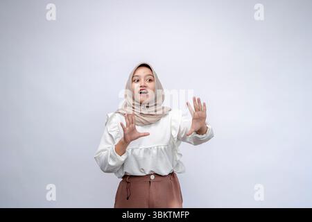 Eine junge indonesische Frau, die Hijab trägt und Stoppschild mit einer Handfläche auf weißem Hintergrund hält Stockfoto