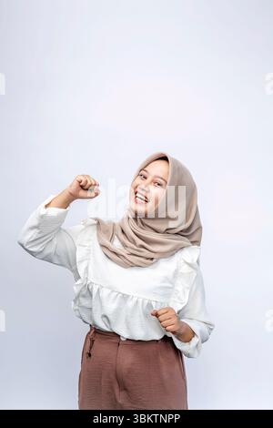 Aufgeregt schöne indonesische muslimische Frau im Hijab feiert Erfolg und blickt auf die Kamera isoliert auf weißem Hintergrund. Menschen religiöse Leben Stockfoto