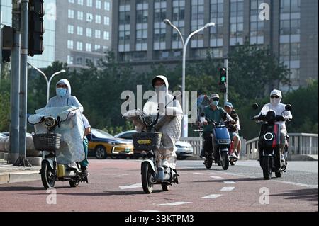 Peking, China. Juni 2025. Mehrere Menschen fahren ihre Motorroller in Jacken, mit Masken und manchmal Sonnenbrillen. In China schützen sich viele Menschen mit langer Kleidung und Gesichtsmasken vor der Sonne - auch um einen hellen Hautton zu erhalten, der in China beliebt ist. Peking ist derzeit von extremer Hitze betroffen. Die Stadtverwaltung warnte die Bewohner der chinesischen Hauptstadt vor Hochtemperaturen von bis zu 38 Grad. In der Folge wurde der Sportunterricht beispielsweise in Schulen und Kindergärten abgesagt. Quelle: Johannes Neudecker/dpa/Alamy Live News Stockfoto