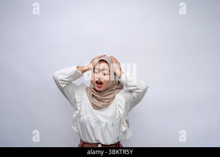 Terminkonzept. Porträt einer schockierten jungen indonesischen Frau, die Hijab trägt und isoliert über der weißen Hintergrundwand des Studios ihren Kopf packt. Gestresst Stockfoto