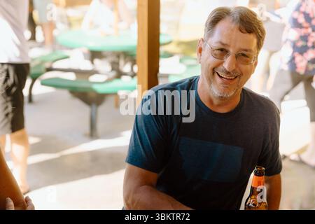 Der Mann lächelt mit Bier in der Hand bei sonnigen Treffen im Freien Stockfoto