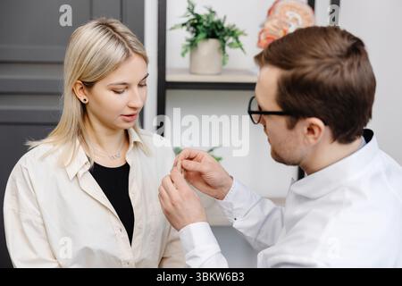 Ein junger attraktiver Hals-Nasen-Ohren-Arzt berät eine Patientin. Ein Arzt erklärt einer Frau, wie man ein Hörgerät trägt. Stockfoto