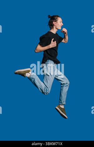 Ein lebhafter und energiegeladener junger Mann läuft fröhlich und genießt unterwegs einen köstlichen Snack Stockfoto