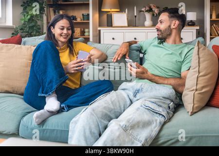 Einfaches Leben, zwei Ziele. Junger Mann und Frau, gerade verheiratet, sitzend und umarmt auf dem Sofa in ihrer neuen Wohnung. Verliebtes Paar, das sich nach Hard D ausruhen lässt Stockfoto
