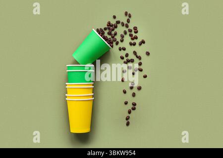 Umgedrehte Einwegbecher mit verstreuten Kaffeebohnen auf grünem Hintergrund Stockfoto