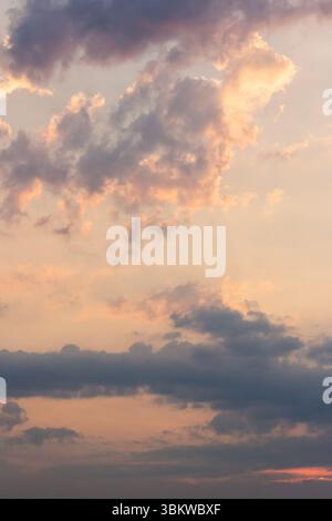 cumulus Wolken am Himmel, vom Wind geweht. Sonnenuntergang stürmisch. Trübe Wettermeteorologie-Hintergrund bei orangenem Schein. Abendstimmung Stockfoto