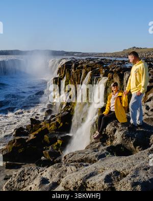 Ein Paar genießt eine atemberaubende Aussicht in der Nähe eines mächtigen Selfoss Wasserfalls in Island. Die Sonne erleuchtet das kaskadierende Wasser, während sie die Natur roh b umarmen Stockfoto