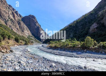 Ein Fluss fließt durch eine zerklüftete Bergschlucht unter einem klaren blauen Himmel. Stockfoto