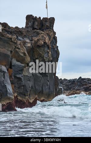 Hohe vulkanische Klippe, die von brechenden Meereswellen an der Küste Teneriffas getroffen wurde Stockfoto