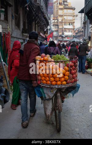 Ein Straßenverkäufer schiebt ein mit Obst beladenes Fahrrad durch eine überfüllte Marktstraße und verkauft frische Produkte. Stockfoto