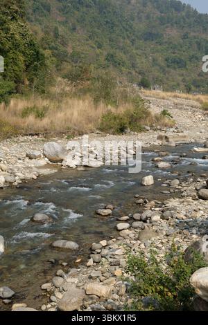 Wasser fließt über Felsen in einem trockenen Flussbett, eine Lebensader durch die Landschaft aus trockenem Gras und bewaldeten Hügeln. Stockfoto
