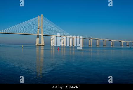 Die Vasco da Gama-Brücke überspannt den Tejo in Lissabon, Portugal und transportiert Fahrzeuge unter klarem blauen Himmel über das Wasser. Stockfoto