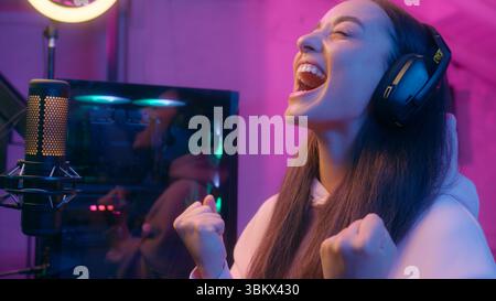 Weißes Mädchen weibliche Frau glückliche Streamer Gamer Gewinner Champion Play Online Match Battle Stream trägt Kopfhörer gewinnt Preiserfolg schreien Stockfoto