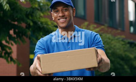 Sorgloser männlicher Arbeiter von Postfracht-Express-Zustellungsmann Guy Kuriermanager lächelnd arbeitend mit Pappkarton Paketstand und Blick auf die Kamera Stockfoto