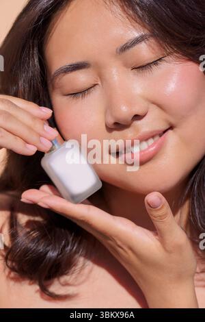 Frau trägt Hautpflegeprodukte auf ihr Gesicht auf, mit einem ruhigen Ausdruck und sanfter Beleuchtung, die die Wichtigkeit von Selbstpflege- und Schönheitsritualen unterstreicht Stockfoto