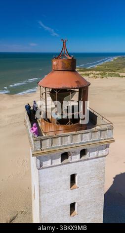 Visitors admire breathtaking views from the top of Rubjerg Knude lighthouse, a historic landmark overlooking the sandy beaches and dunes of Denmark. Stockfoto