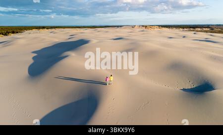 Schlendern Sie durch die bezaubernde Landschaft Dänemarks, wo sich die weichen Sanddünen endlos unter einem lebendigen Himmel erstrecken. Zwei Figuren schlendern entlang der Dünen, Rabjerg Mile Dunes, Dänemark. Stockfoto