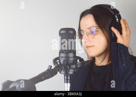 Junge kaukasische Frau im Studio mit Mikrofon und Kopfhörern. Stockfoto