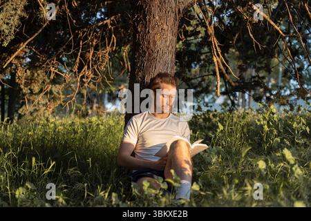 Ein Mann liest ein Buch friedlich in einem sonnigen Park Stockfoto