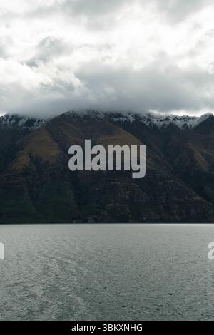 Moody Wolken ziehen sich über zerklüftete, schneebedeckte Gipfel, während ein kalter See die ruhige Intensität der Natur widerspiegelt und Einsamkeit, Ehrfurcht und die erhabene Kraft von Unt weckt Stockfoto