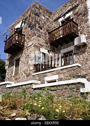 Rustikale mediterrane Hausfassade mit Steinmauer, Holzbalkonen und trockenem Gras darunter, die an ländlichen Sommercharme erinnern. Stockfoto