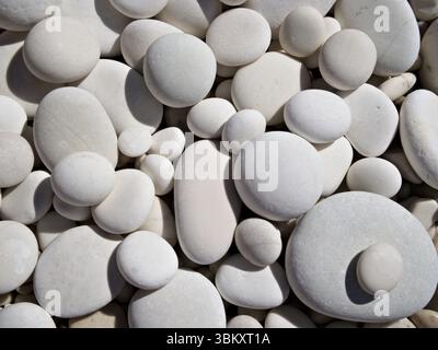 Nahaufnahme von weißen, glatten Kieselsteinen, die einen beruhigenden natürlichen Texturhintergrund bilden. Stockfoto
