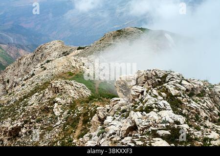 Zerklüfteter Bergkamm, teilweise bedeckt von Wolken und Nebel. Chimgan Mountains, Usbekistan. Juni 2025 Stockfoto