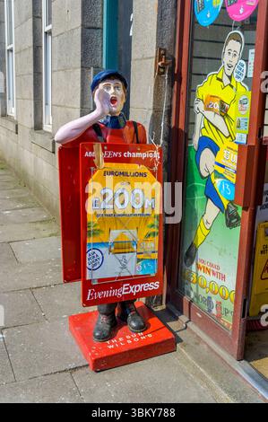 Vintage-Newsboy-Statue auf einem Gehweg neben einem Zeitungsladen, der die Aberdeen Evening Express-Zeitung in Aberdeen, Schottland, Großbritannien, Europa anpreist Stockfoto