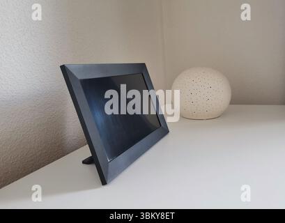 Schwarzes Modell mit digitalem Fotorahmen mit einem Kopierraum auf weißer Arbeitsplatte mit dekorativer kugelförmiger Lampe Stockfoto