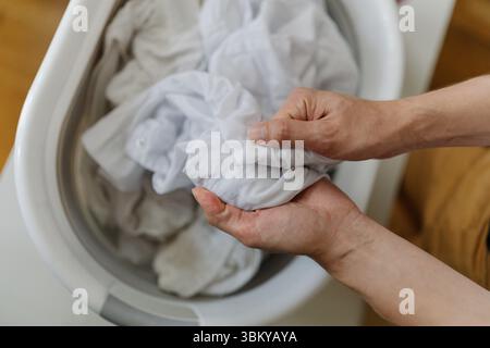 Hochwinkelansicht eines jungen Mannes, der weiße Kleidung zum Waschen vorbereitet, in einem Becken mit Fleckenentferner einweicht, bevor er sie in die Waschmaschine für stellt Stockfoto