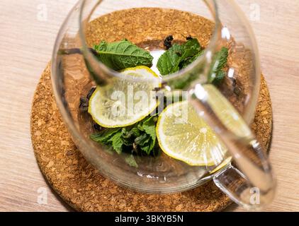Stilvolle transparente Teekanne mit getrockneten Teeblättern, Minzblättern und Zitronenscheiben Stockfoto