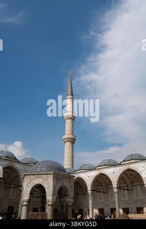 Eine Niedrigwinkelaufnahme der Blauen Moschee in Istanbul, Türkei, mit ihren architektonischen Details, einschließlich Kuppeln, Bögen und einem hohen Minarett vor einem blauen Himmel mit verstreuten Wolken. Stockfoto