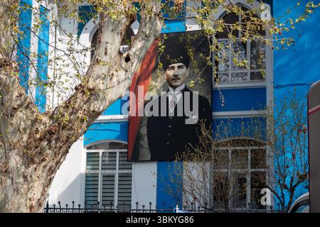 Ein Porträt von Mustafa Kemal Atatürk, dem Gründer der Republik Türkei, hängt an der Seite eines blau-weißen Gebäudes, eingerahmt von einem Baum. Stockfoto