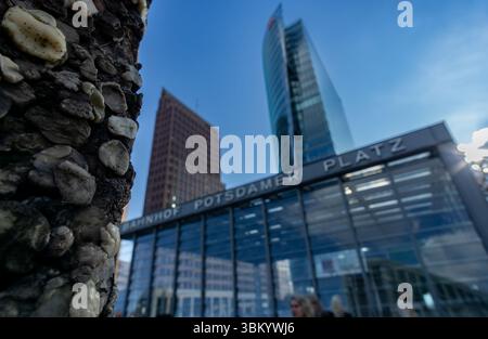Scharfer Fokus auf ein Berliner Mauer-Segment mit verschwommenem Potsdamer Platz und urbaner Menschenmenge im Hintergrund. Stockfoto