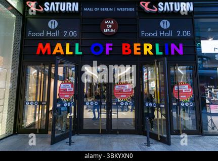 Farbenfroher Eingang der Mall of Berlin mit Regenbogenbeschriftung, Saturn-Geschäft und Menschen, die das Einkaufszentrum betreten. Stockfoto