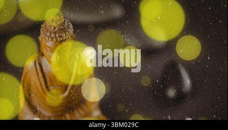 Glühende gelbe Lichter, die auf dem Tisch neben geschnitzter hölzerner Buddha-Statue und schwarz poliertem Kieselstein schweben Stockfoto