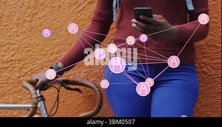 Eine Frau, die das Smartphone mit Fahrrad und Netzwerküberlagerung gegen die orangene Wand hält Stockfoto