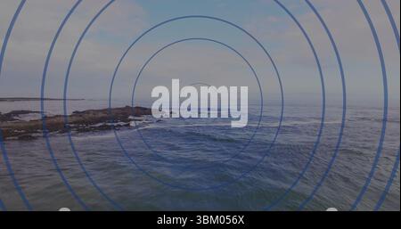 Erfassen Sie die felsige Küste aus der Drohnenansicht und zeigen Sie blaue konzentrische Kreise über dem Ozean Stockfoto