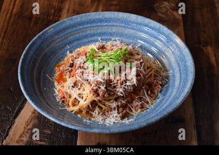 Blaue Schüssel mit Pasta Bolognese garniert mit grünen Sprossen Stockfoto