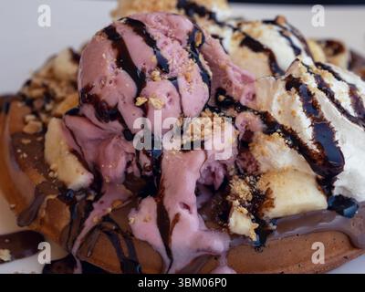 Dekadente Waffel mit Erdbeeren- und Vanilleeis, Schlagsahne, Bananen, Schokoladensauce und Nüssen Stockfoto