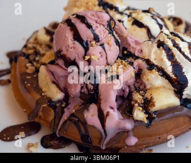 Dekadente Waffel mit Erdbeeren- und Vanilleeis, Schlagsahne, Bananen, Schokoladensauce und Nüssen Stockfoto